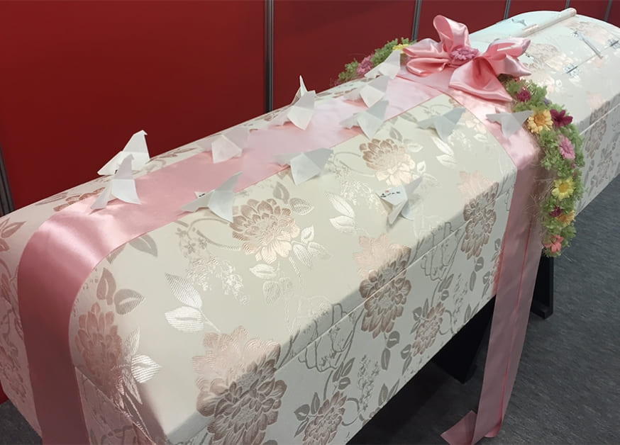 ピンクのリボンとおくりバトで飾られたOKURIBATOの棺桶
